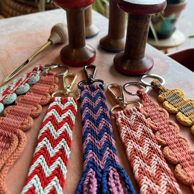 Colourful ply-split braided keychains on a table with wooden spools and a grip fid tool in the background