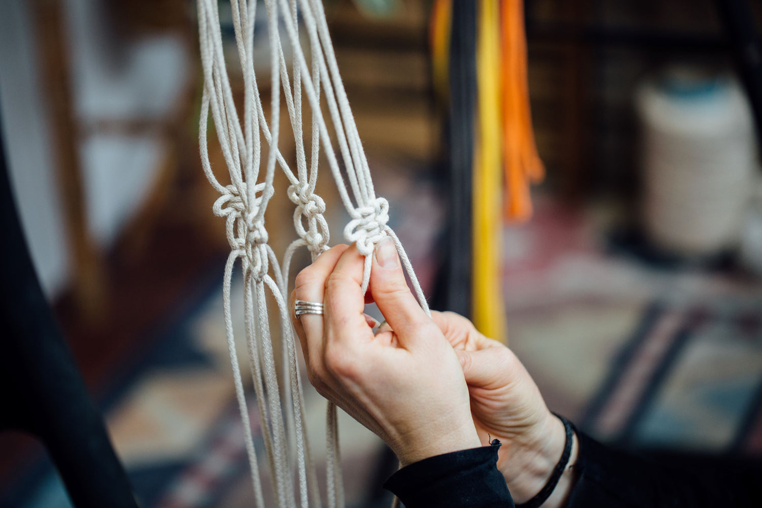 Close-up of hands tying knots in a macrame project with a blurred background