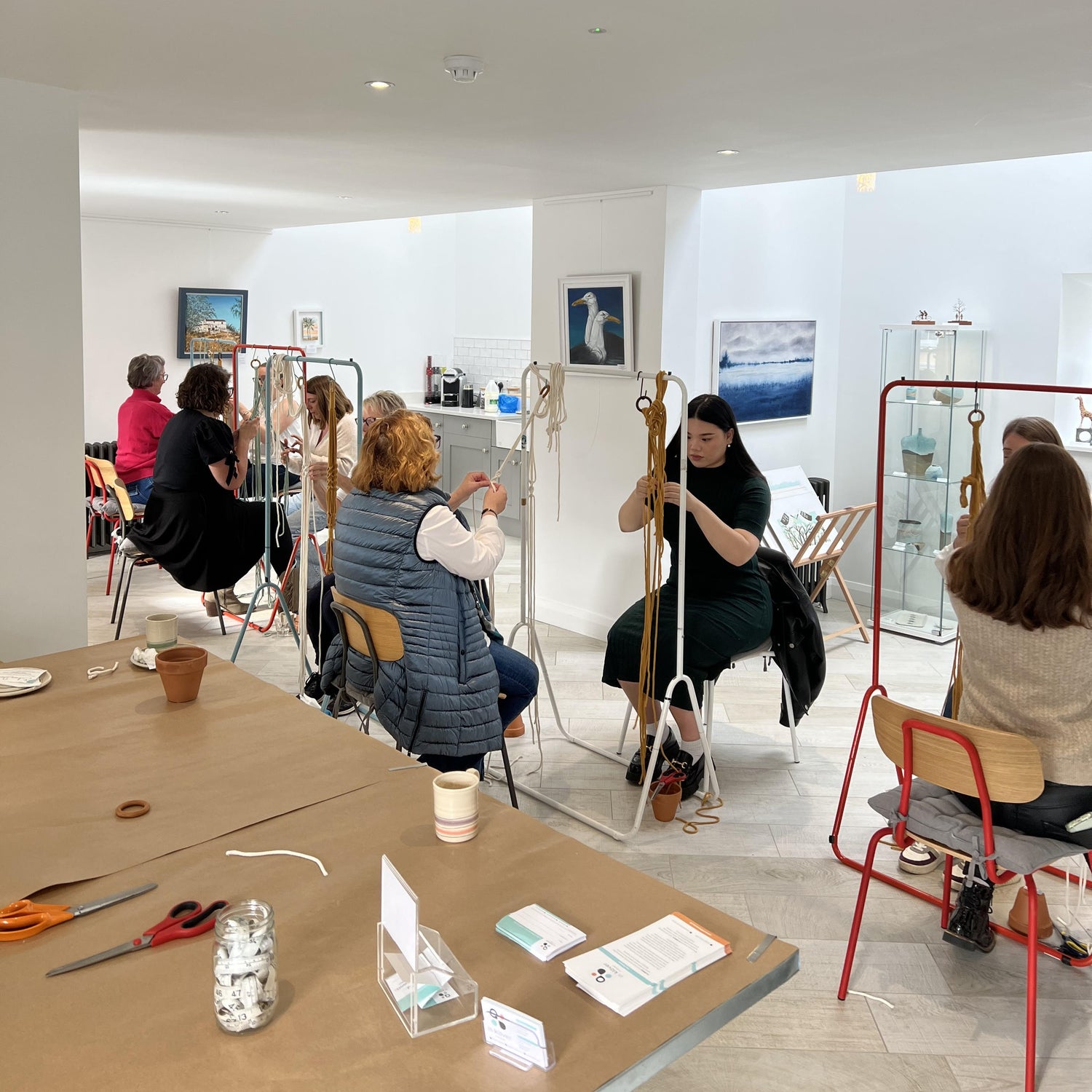 Art studio with a group of focused people sitting at rails, tying knots with coloured cords.